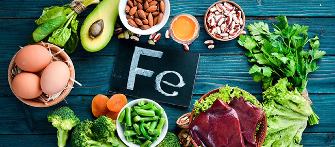 Food containing natural iron. Fe: Liver, avocado, broccoli, spinach, parsley, beans, nuts, on a blue background. Top view.